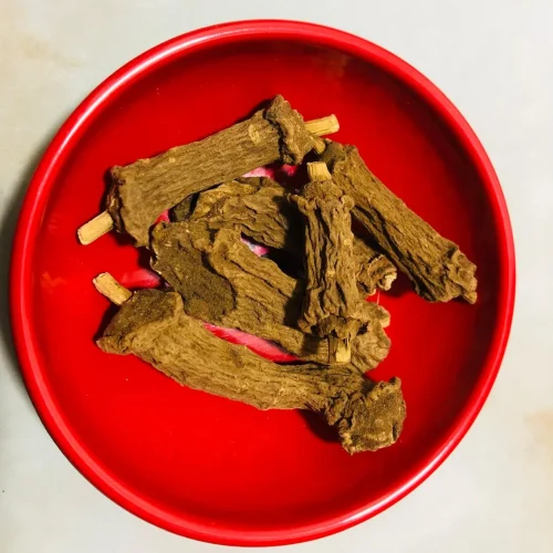 Close-up of dried, reddish-brown Iramusu (Hemidesmus indicus) roots or stem pieces, showing their distinctive texture and aromatic qualities.